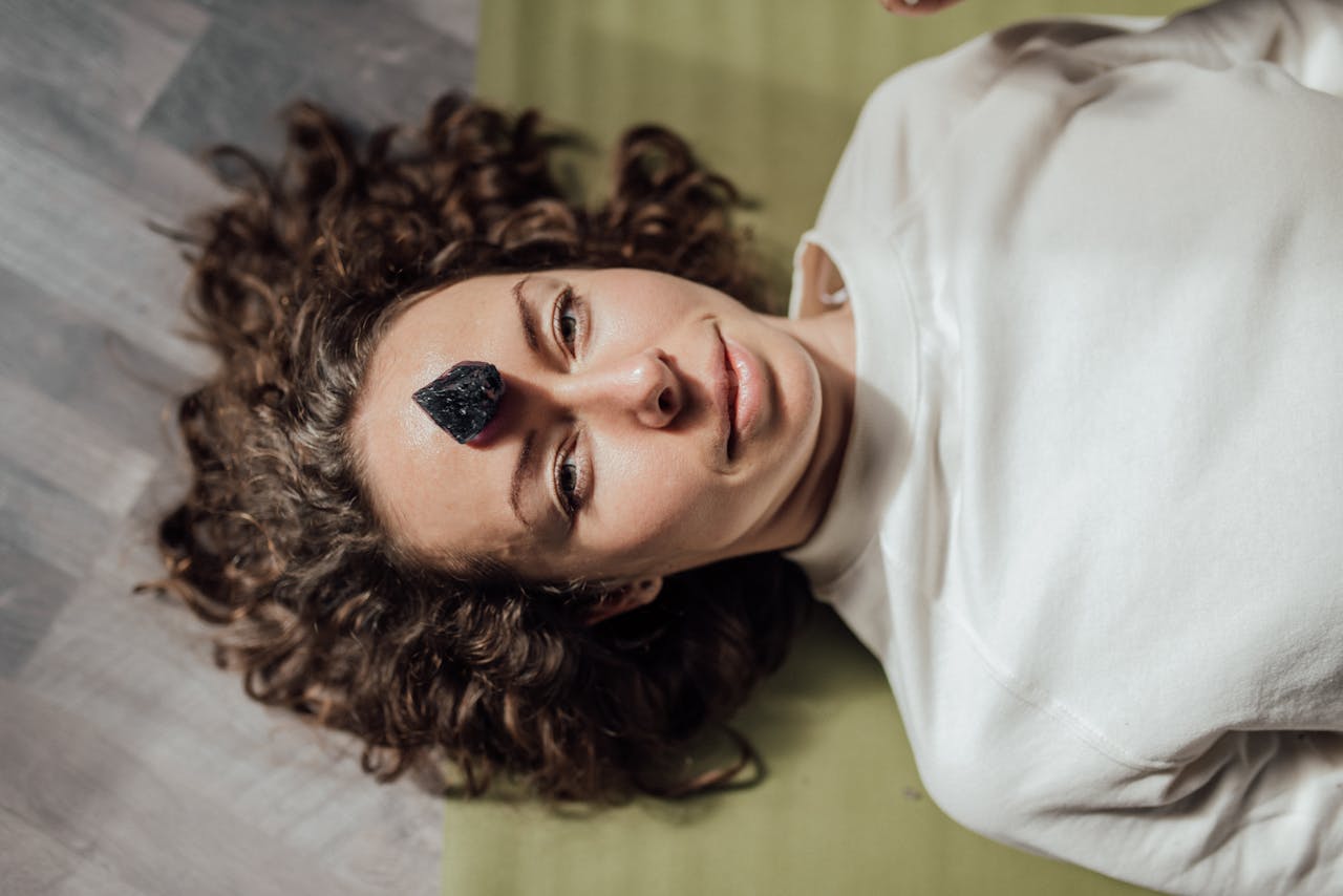 services-03 Young woman lying down with a healing crystal on her forehead, promoting relaxation and meditation.