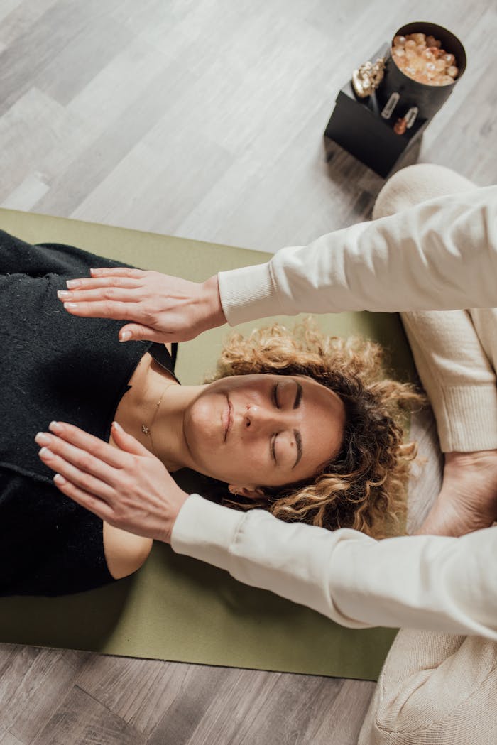 services-02 A woman receiving Reiki therapy with hands hovering over her, eyes closed, in a serene indoor setting.